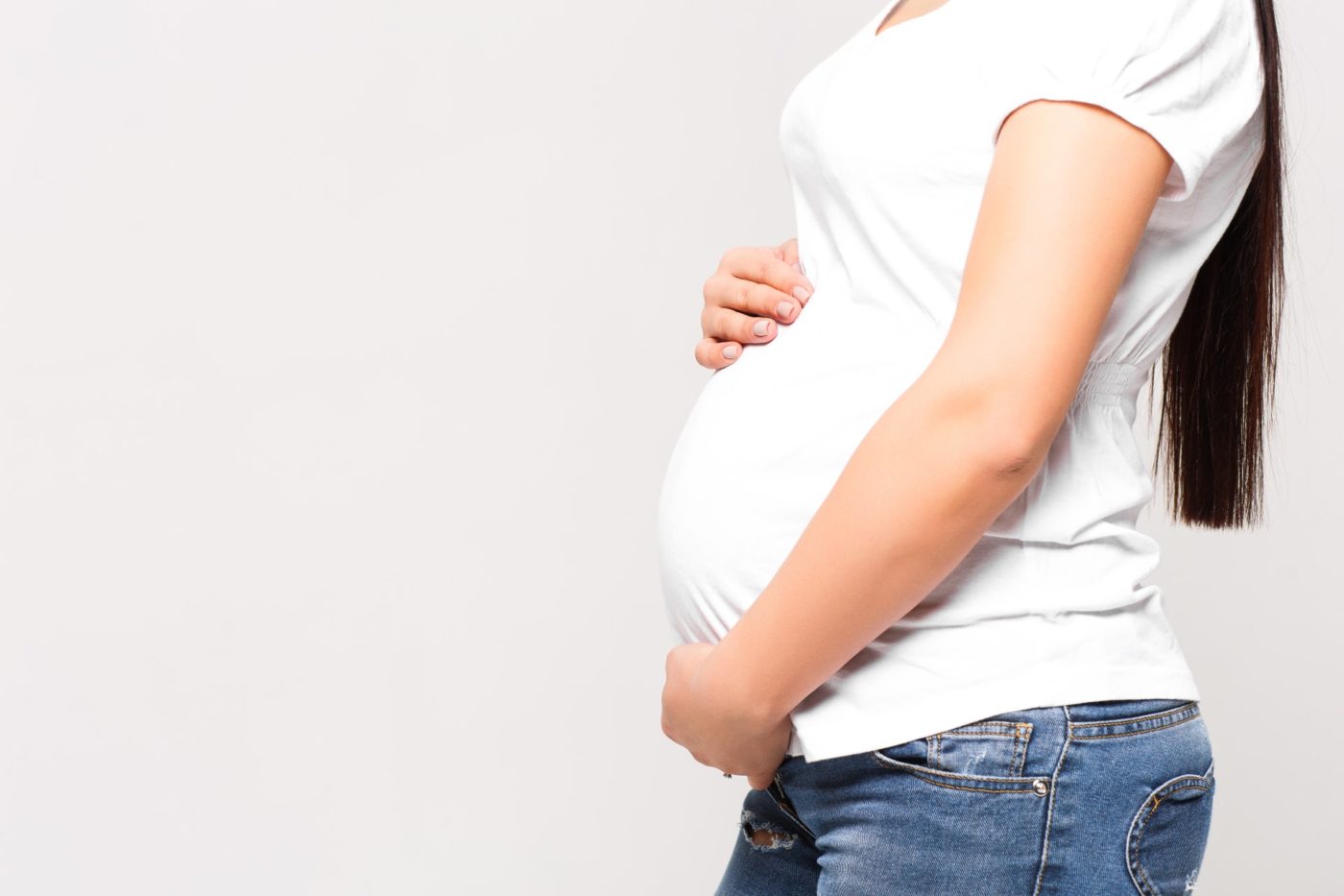 gros plan femme enceinte meconnaissable mains ventre au mur blanc 1